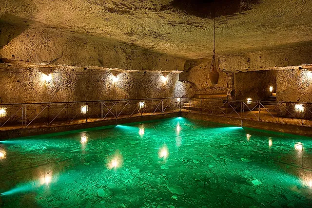 Eine Zisterne aus der Renaissance mit sanft beleuchtetem grünem Wasser in der Galleria Borbonica, Neapel